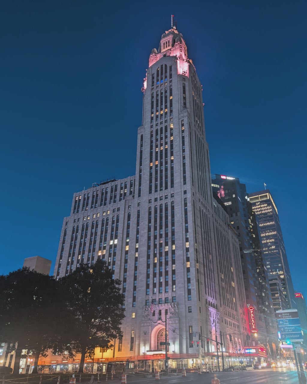 The LeVeque Tower, a pale giant against the bruised velvet sky, watches over the city's sleepless soul, its secrets laid bare in the neon glow.
